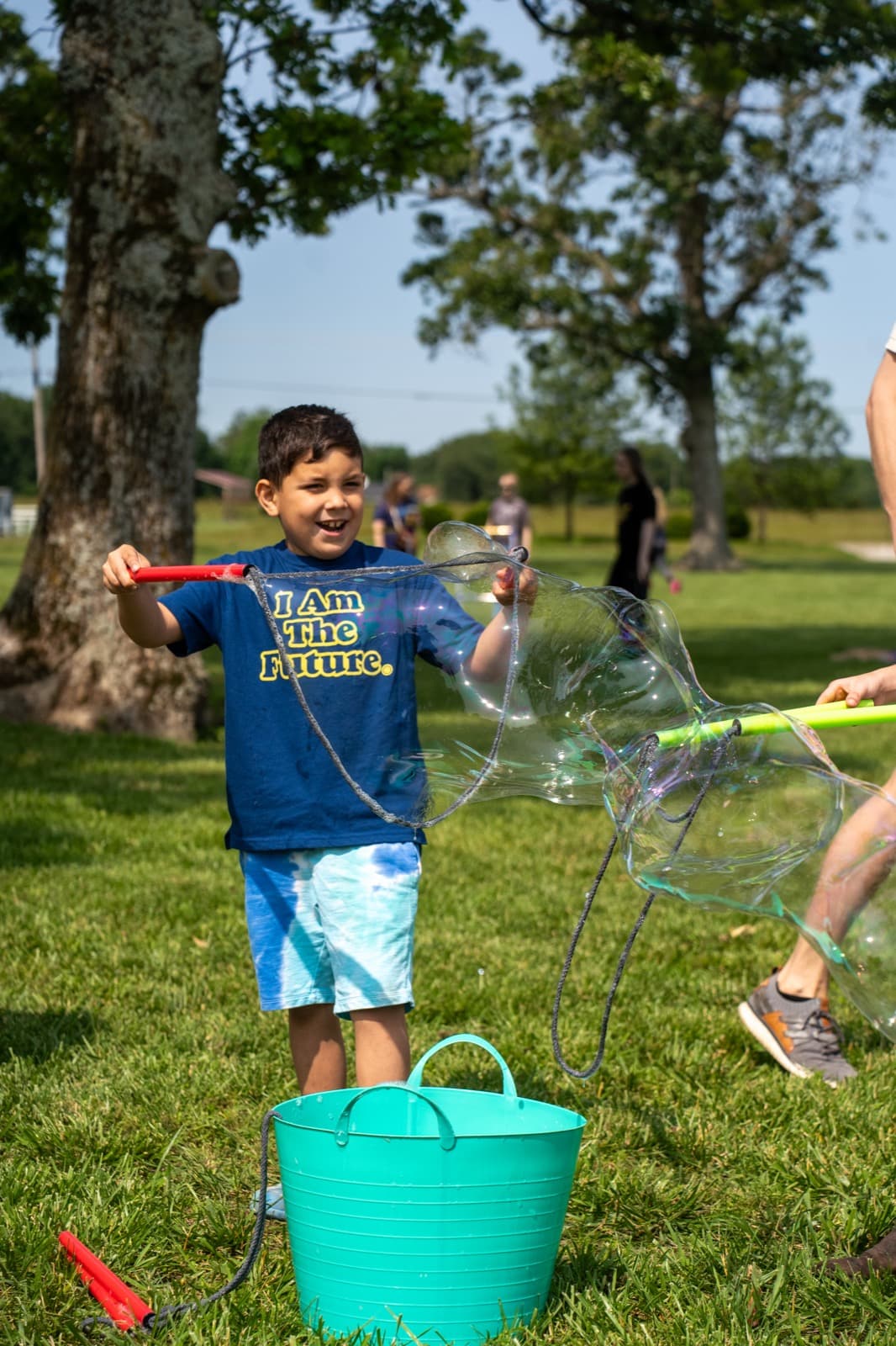 A child smiles while holding a bubble wand at an outdoor activity station.