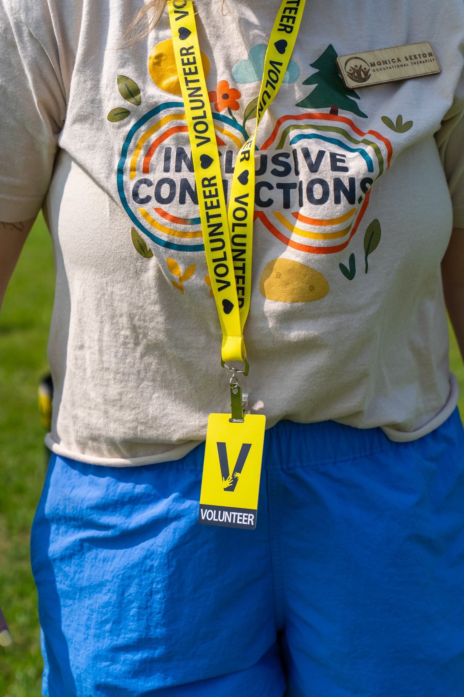 Close-up of a volunteer wearing an Inclusive Connections lanyard and badge at a community event.